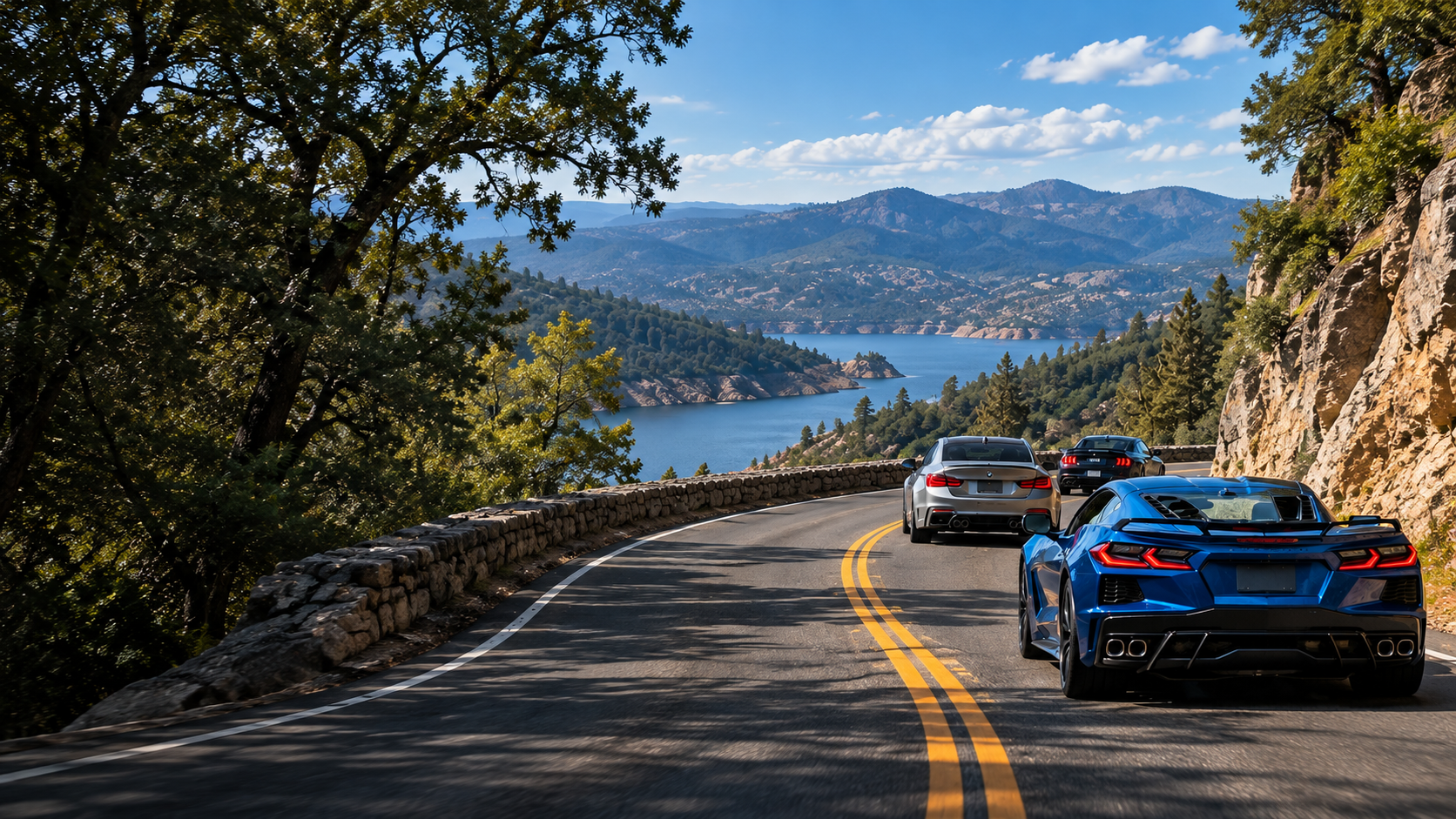 Sports cars driving a mountain road above a lake