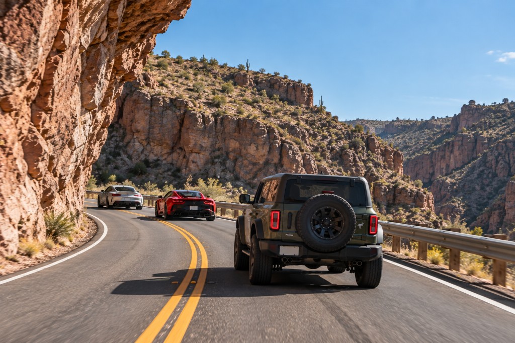 A green Bronco leading cars along a cliff road in Red Rock Canyon
