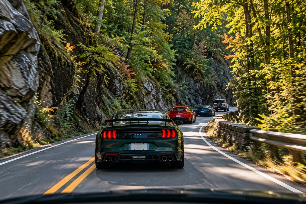 A green Mustang leading cars along a forest road in the Smoky Mountains